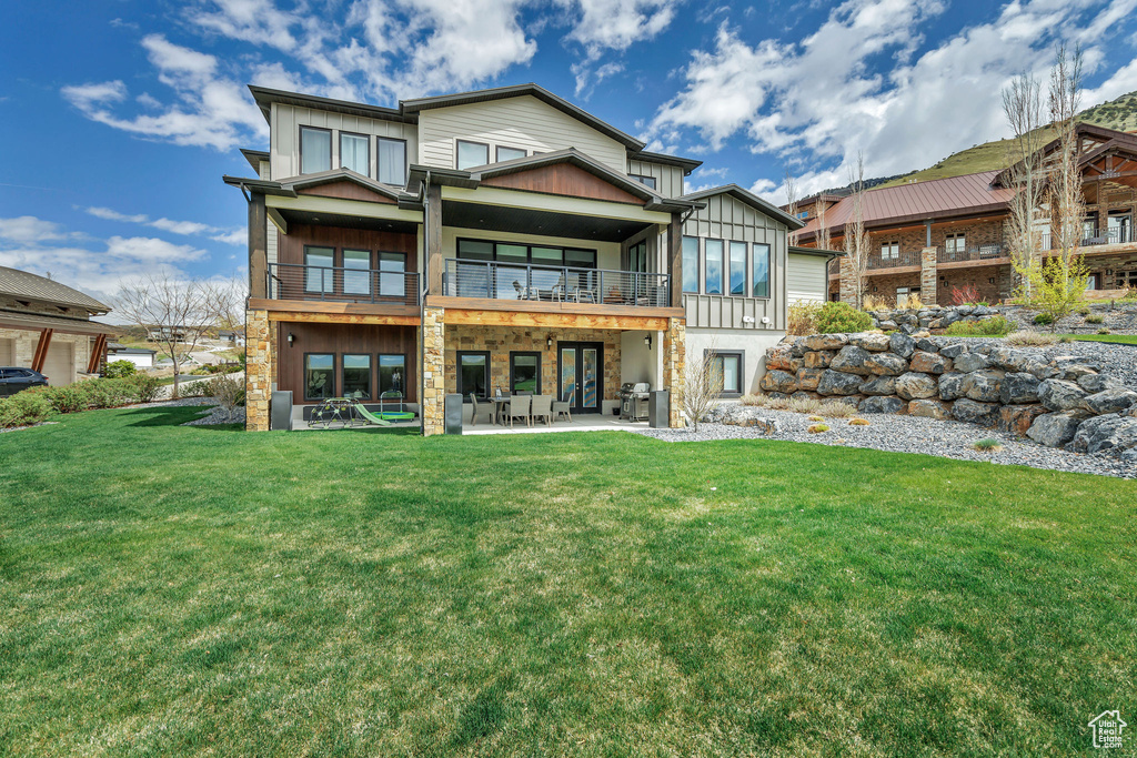 Rear view of property featuring a balcony, stone siding, a patio, board and batten siding, and a yard
