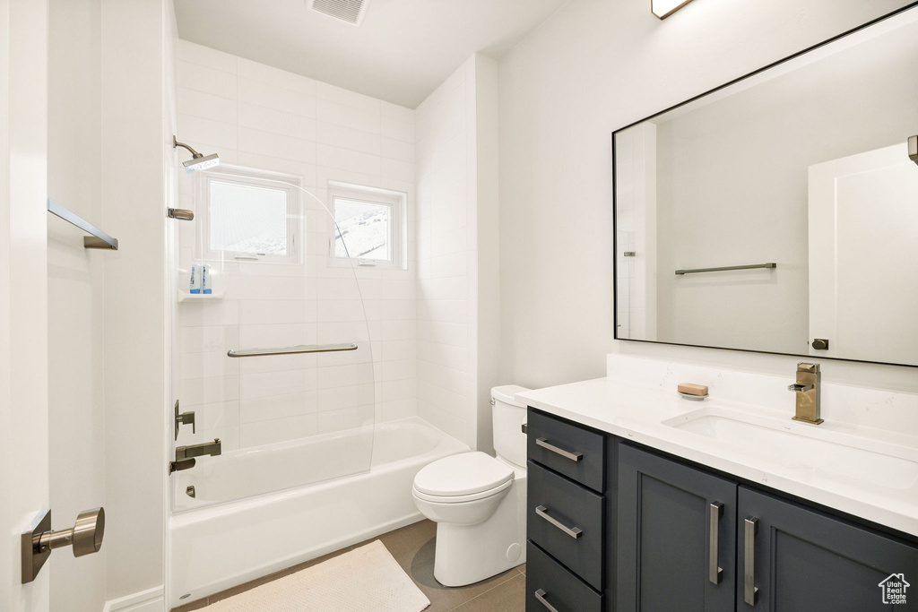 Full bathroom with tile patterned floors, toilet, vanity, and tiled shower / bath combo