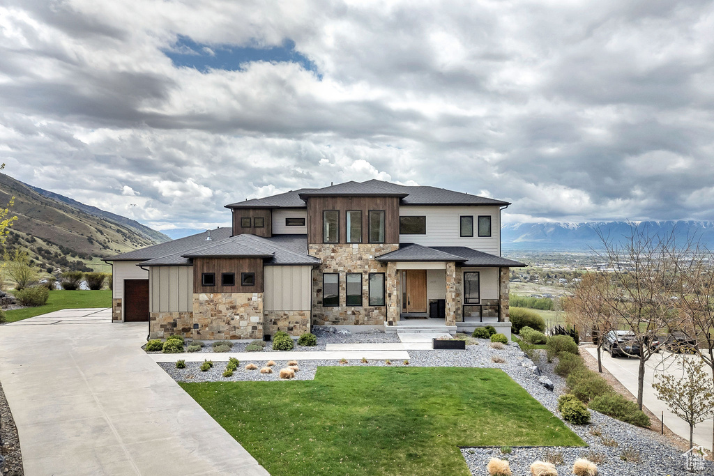 Prairie-style home featuring a porch, driveway, a garage, a front lawn, and stone siding