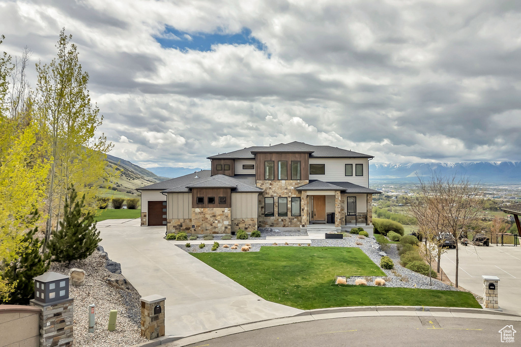 Prairie-style home featuring a front lawn, stone siding, board and batten siding, a mountain view, and driveway