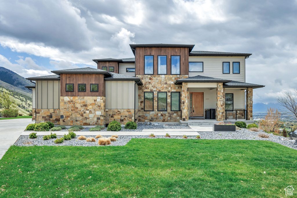 View of front facade featuring covered porch, a mountain view, stone siding, and a front lawn
