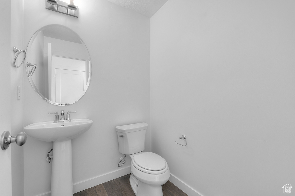 Half bath featuring wood finished floors, toilet, baseboards, and a sink