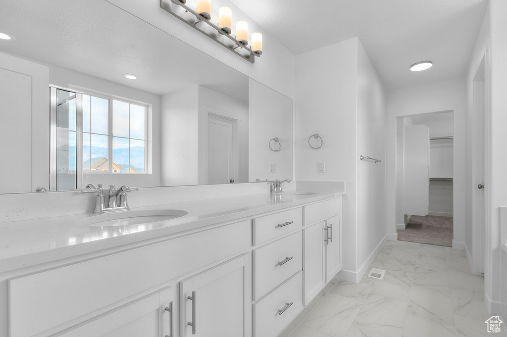 Full bathroom with marble look tile flooring, baseboards, double vanity, a walk in closet, and recessed lighting