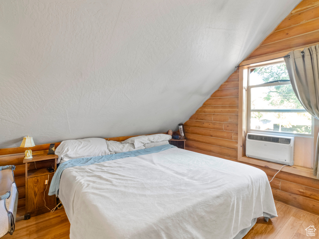 Bedroom with a textured ceiling, lofted ceiling, light hardwood / wood-style floors, and rustic walls