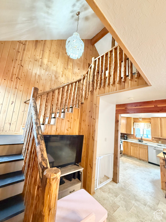 Stairs with lofted ceiling with beams, wood walls, and a notable chandelier