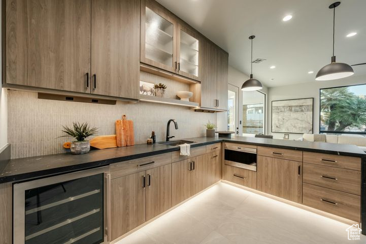 Kitchen featuring wine cooler, sink, backsplash, light brown cabinetry, and pendant lighting