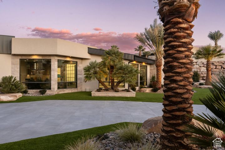 Back house at dusk featuring a patio area and a lawn