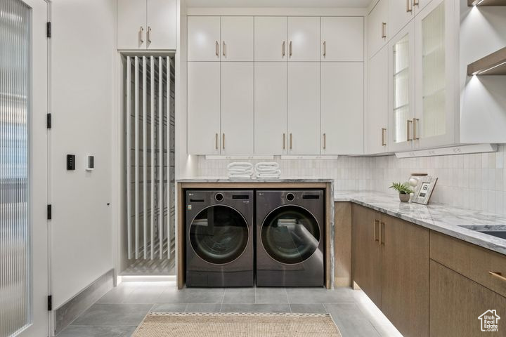 Laundry area with light tile patterned flooring, cabinets, and washing machine and clothes dryer