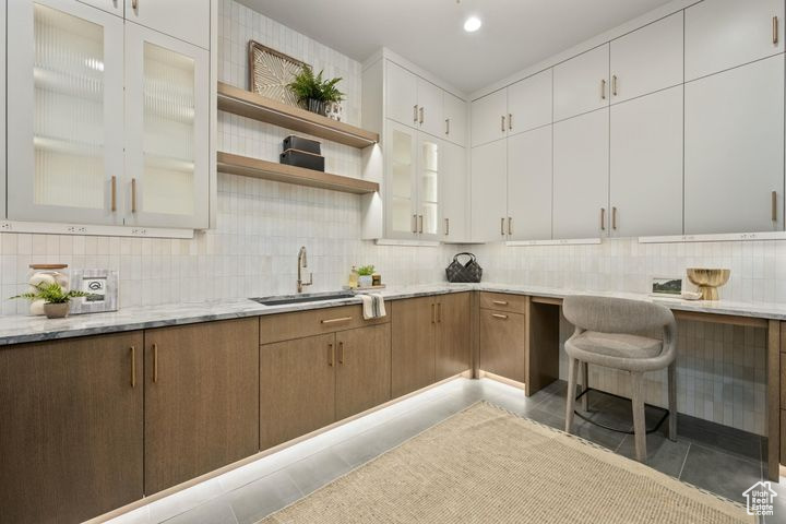 Kitchen featuring light stone counters, decorative backsplash, light tile patterned floors, sink, and white cabinetry