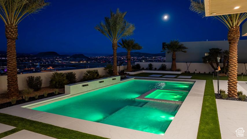 Pool at night featuring an in ground hot tub