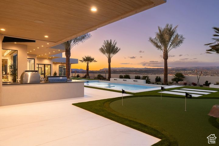 Pool at dusk with an in ground hot tub, a patio, an outdoor kitchen, and grilling area