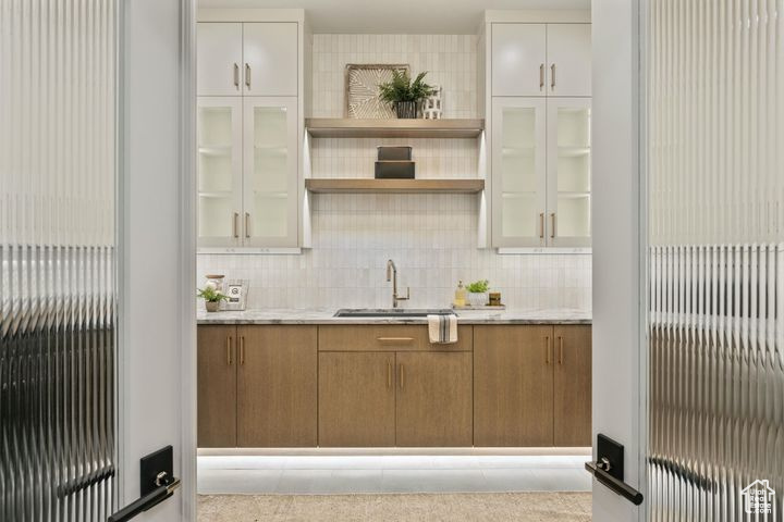 Bar featuring white cabinets, sink, and backsplash
