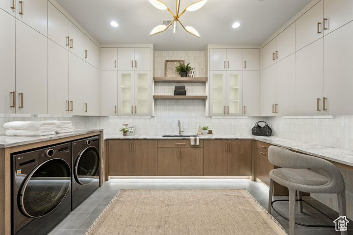 Kitchen with white cabinetry, sink, separate washer and dryer, and light stone counters