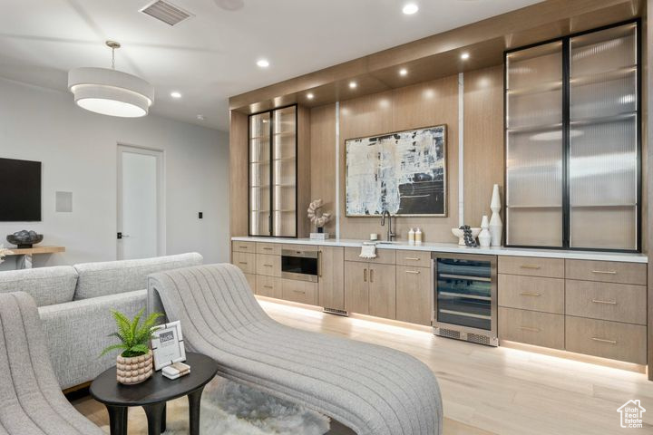 Bar with hanging light fixtures, wine cooler, light hardwood / wood-style floors, sink, and light brown cabinets