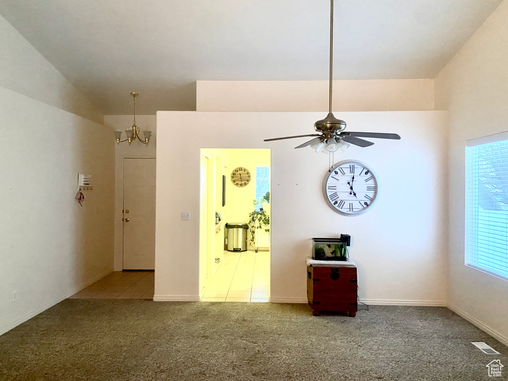 Empty room featuring light carpet, baseboards, visible vents, and ceiling fan with notable chandelier