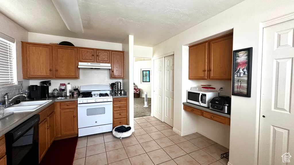 Kitchen with white appliances, under cabinet range hood, brown cabinets, and a sink