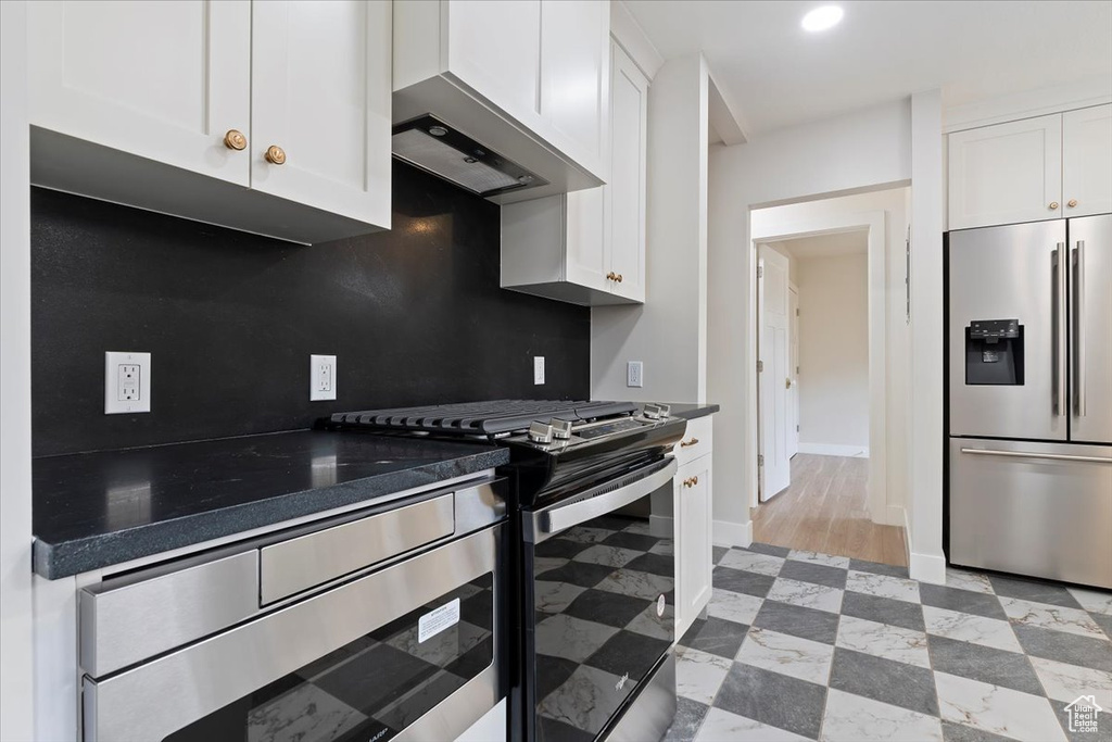 Kitchen featuring white cabinets, appliances with stainless steel finishes, wall chimney range hood, and tasteful backsplash