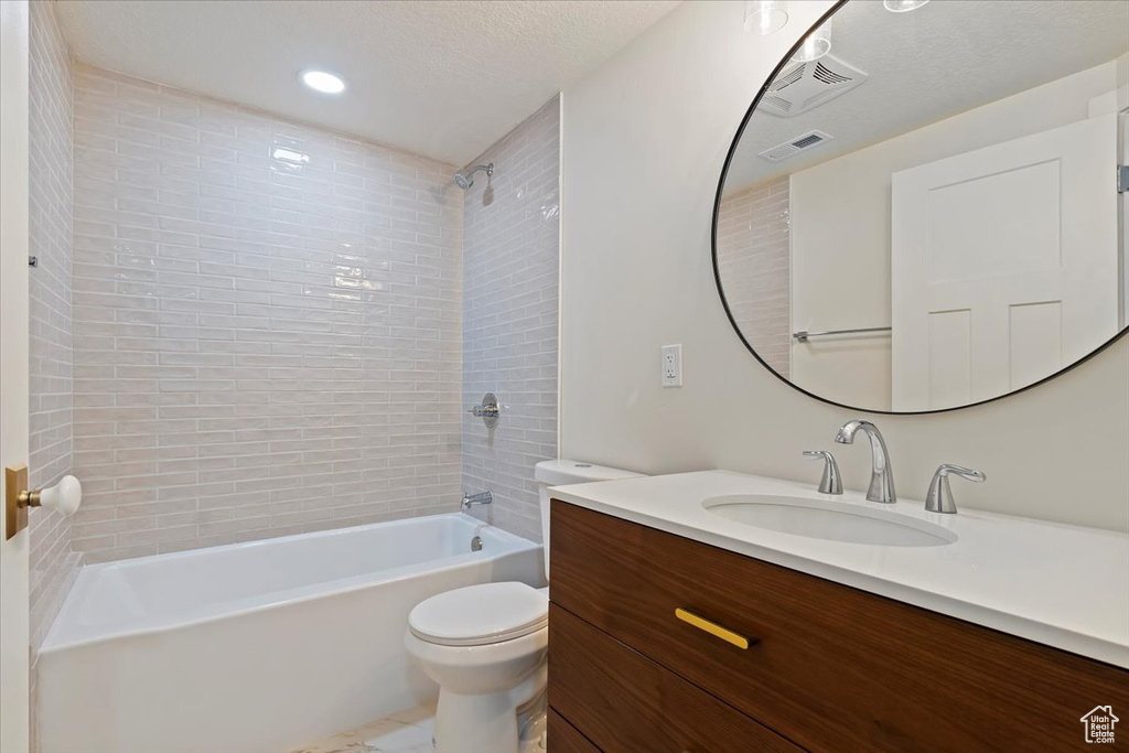 Full bathroom featuring tiled shower / bath combo, vanity, toilet, and a textured ceiling