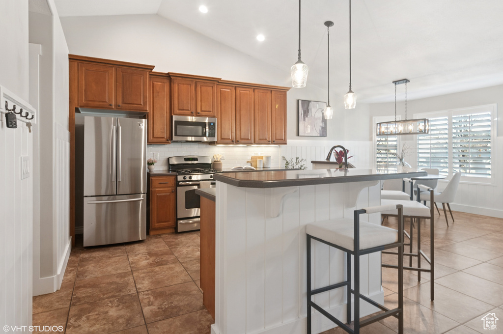 Kitchen featuring a kitchen bar, dark countertops, a center island, stainless steel appliances, and brown cabinetry