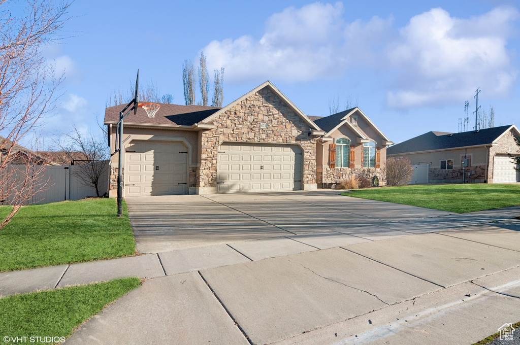 Ranch-style house featuring a front yard, fence, driveway, stone siding, and a garage