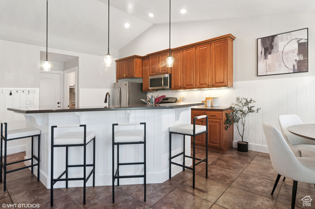 Kitchen with a breakfast bar area, brown cabinetry, vaulted ceiling, appliances with stainless steel finishes, and dark countertops