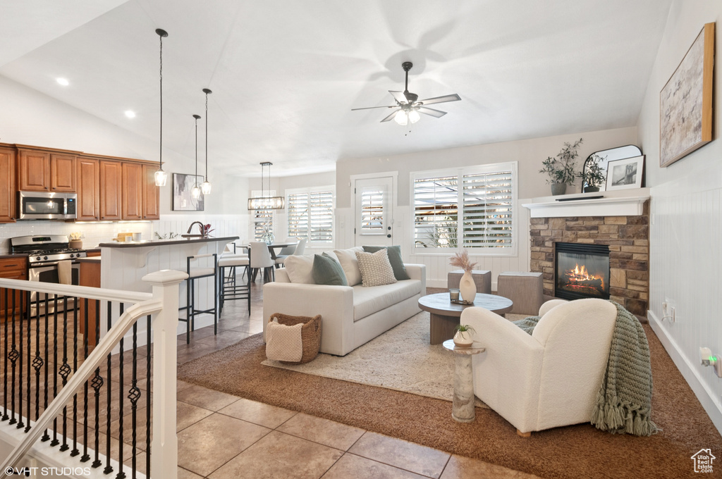 Living area with vaulted ceiling, light tile patterned floors, a stone fireplace, ceiling fan with notable chandelier, and recessed lighting