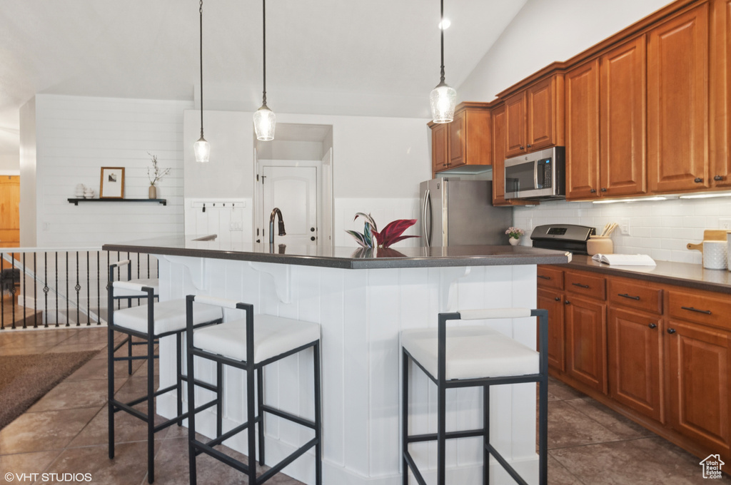 Kitchen featuring a breakfast bar area, vaulted ceiling, appliances with stainless steel finishes, dark countertops, and backsplash
