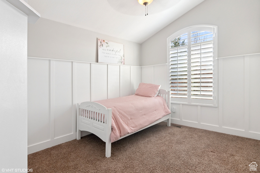 Bedroom featuring a ceiling fan, a wainscoted wall, carpet floors, lofted ceiling, and a decorative wall