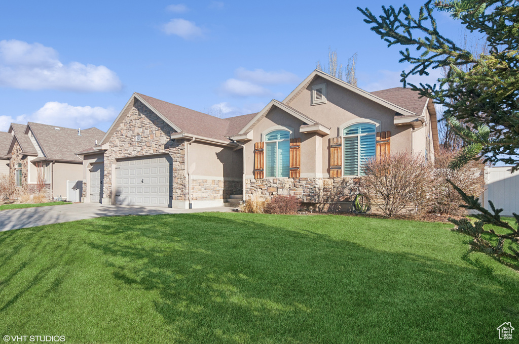 View of front of home with stucco siding, driveway, a front lawn, stone siding, and a garage
