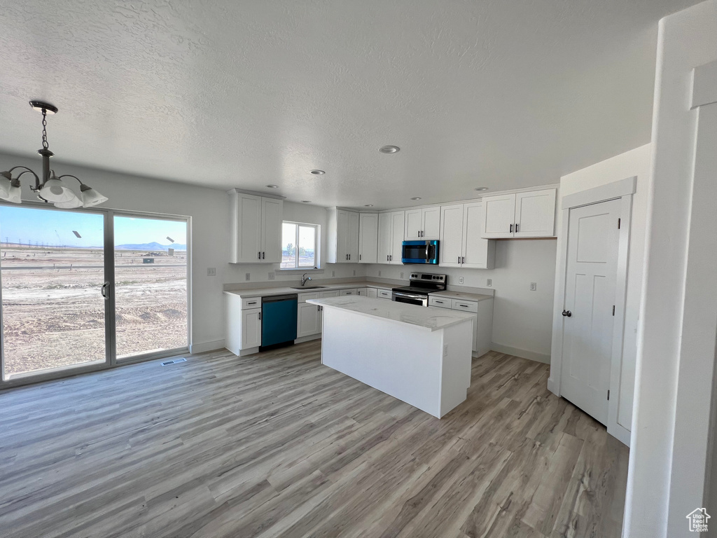 Kitchen featuring hanging light fixtures, stainless steel appliances, a kitchen island, sink, and white cabinetry