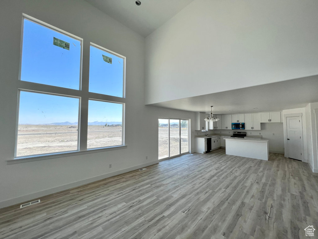 Unfurnished living room featuring a notable chandelier, light hardwood / wood-style floors, a mountain view, and a high ceiling
