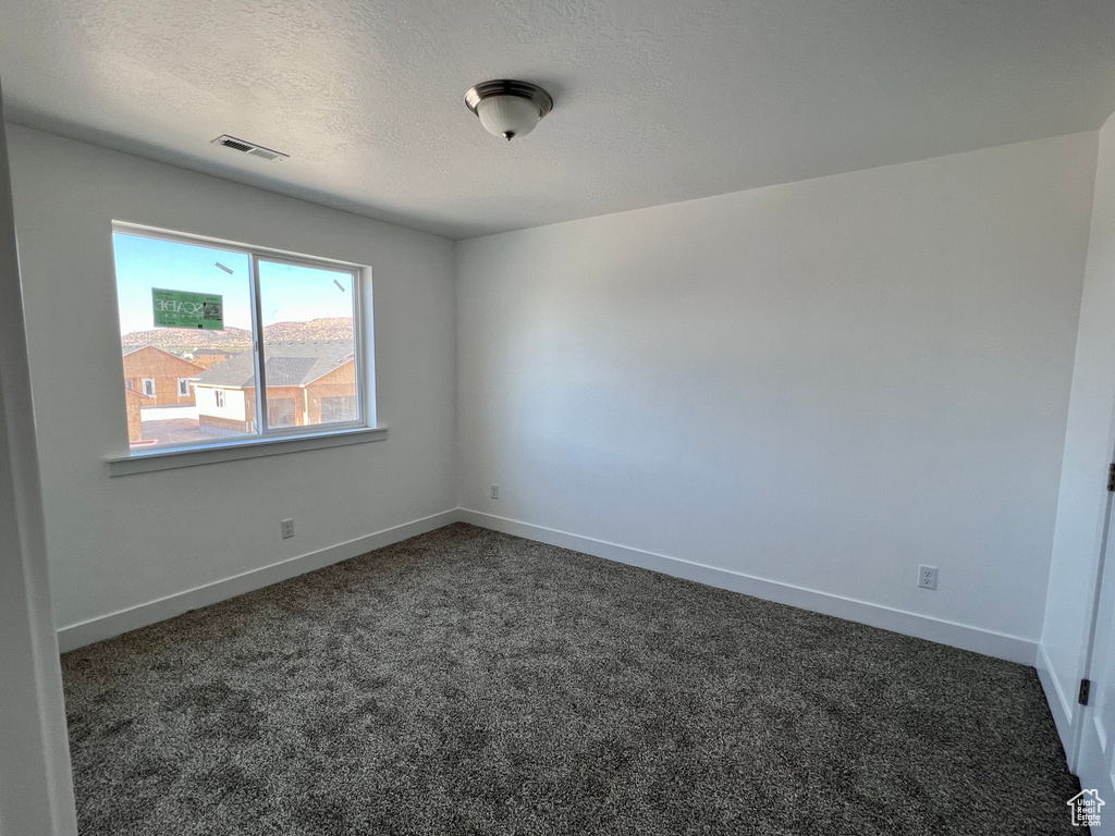 Unfurnished room featuring dark carpet and a textured ceiling