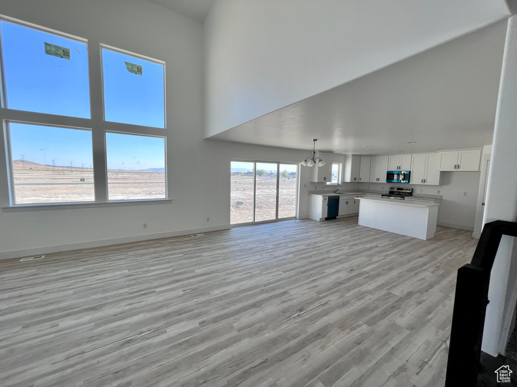 Unfurnished living room with a high ceiling, light wood-type flooring, and an inviting chandelier