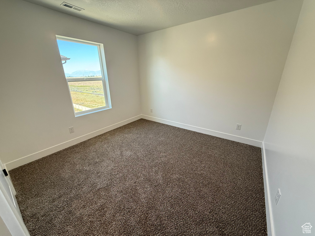 Unfurnished room with baseboards, dark colored carpet, and a textured ceiling