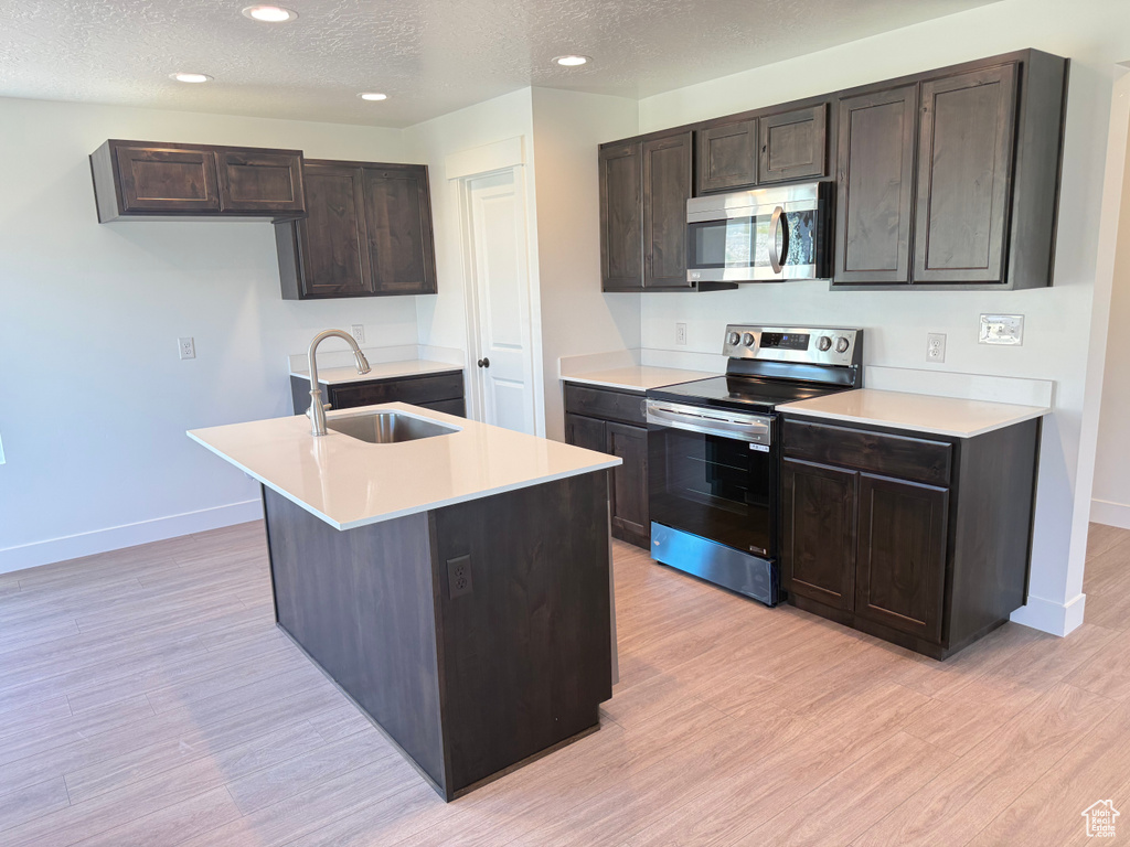 Kitchen featuring appliances with stainless steel finishes, a sink, baseboards, a textured ceiling, and light wood-type flooring
