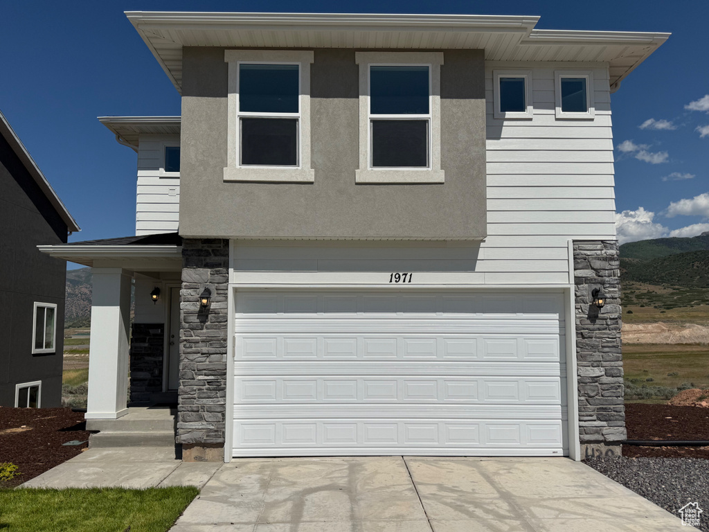 View of front of house featuring stone siding, an attached garage, driveway, and a mountain view