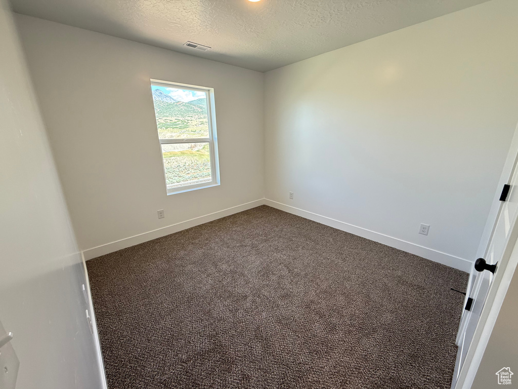 Spare room featuring a textured ceiling, dark colored carpet, and baseboards