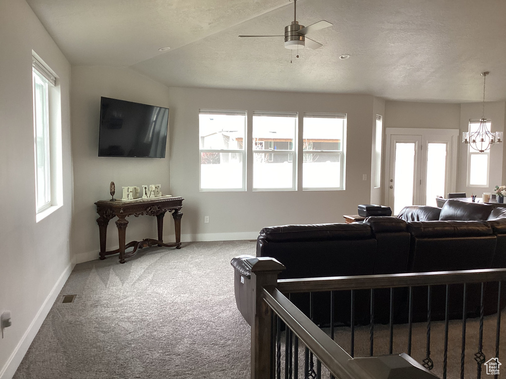 Living room featuring ceiling fan with notable chandelier, lofted ceiling, carpet flooring, and a textured ceiling