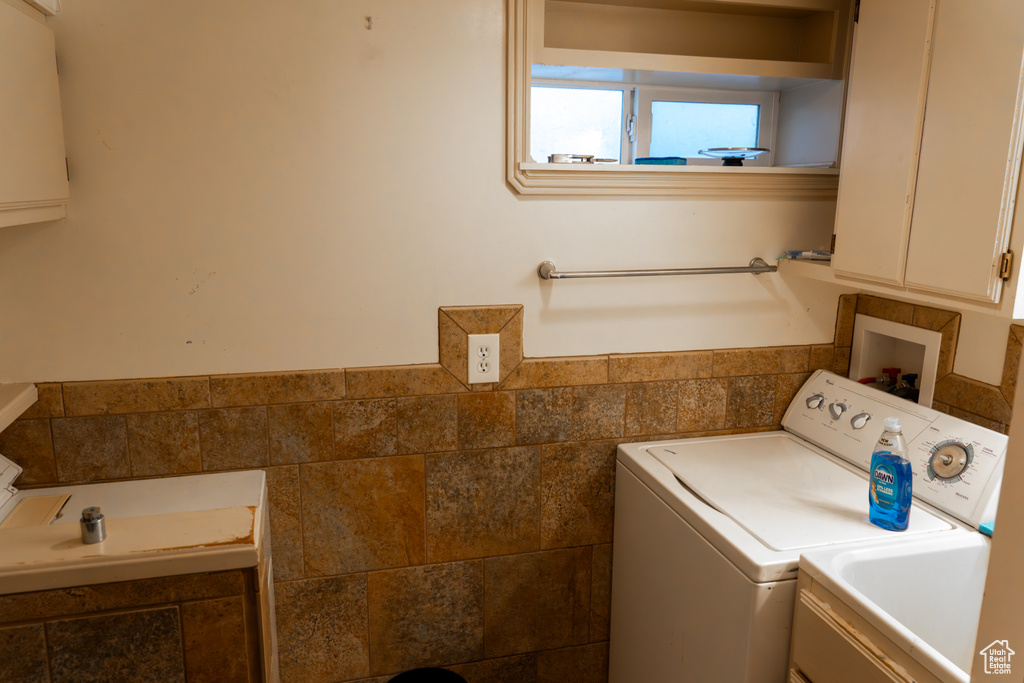 Laundry area with tile walls, sink, and washer and clothes dryer