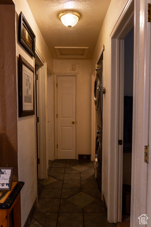 Corridor featuring stacked washing maching and dryer, a textured ceiling, and dark tile patterned floors