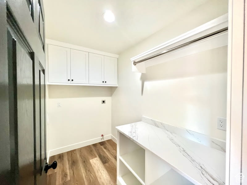 Laundry area featuring light wood-type flooring, cabinets, and electric dryer hookup