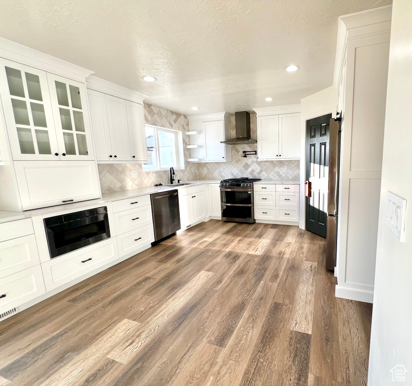 Kitchen with sink, appliances with stainless steel finishes, white cabinets, and wall chimney range hood