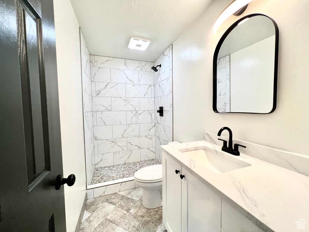 Bathroom with tiled shower, vanity, and toilet