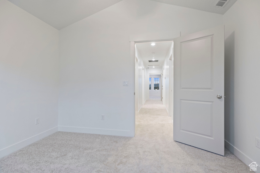 Empty room with light carpet, vaulted ceiling, and baseboards