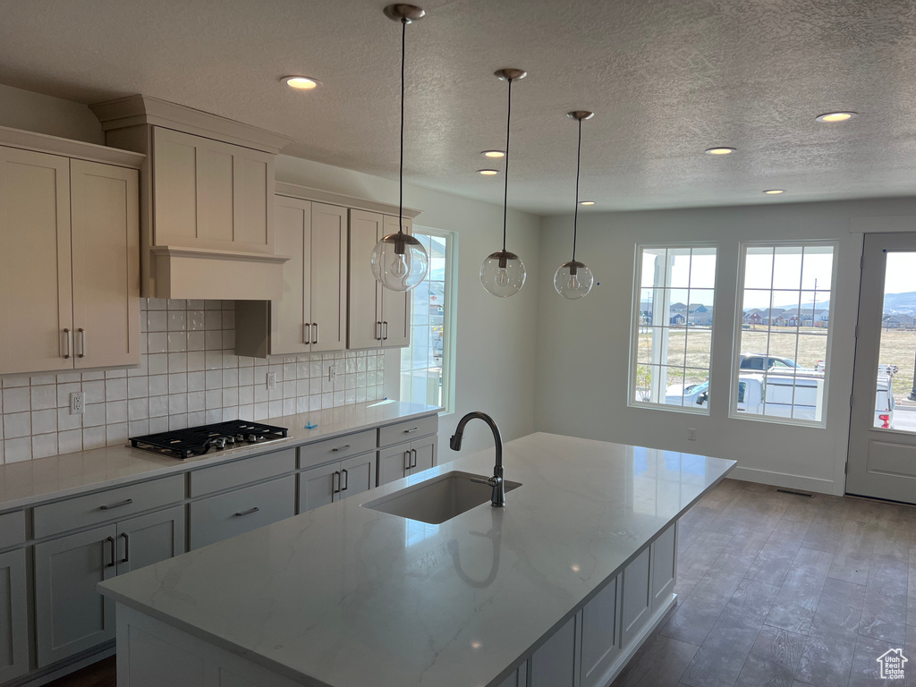 Kitchen with an island with sink, light stone countertops, stainless steel gas stovetop, a sink, and backsplash