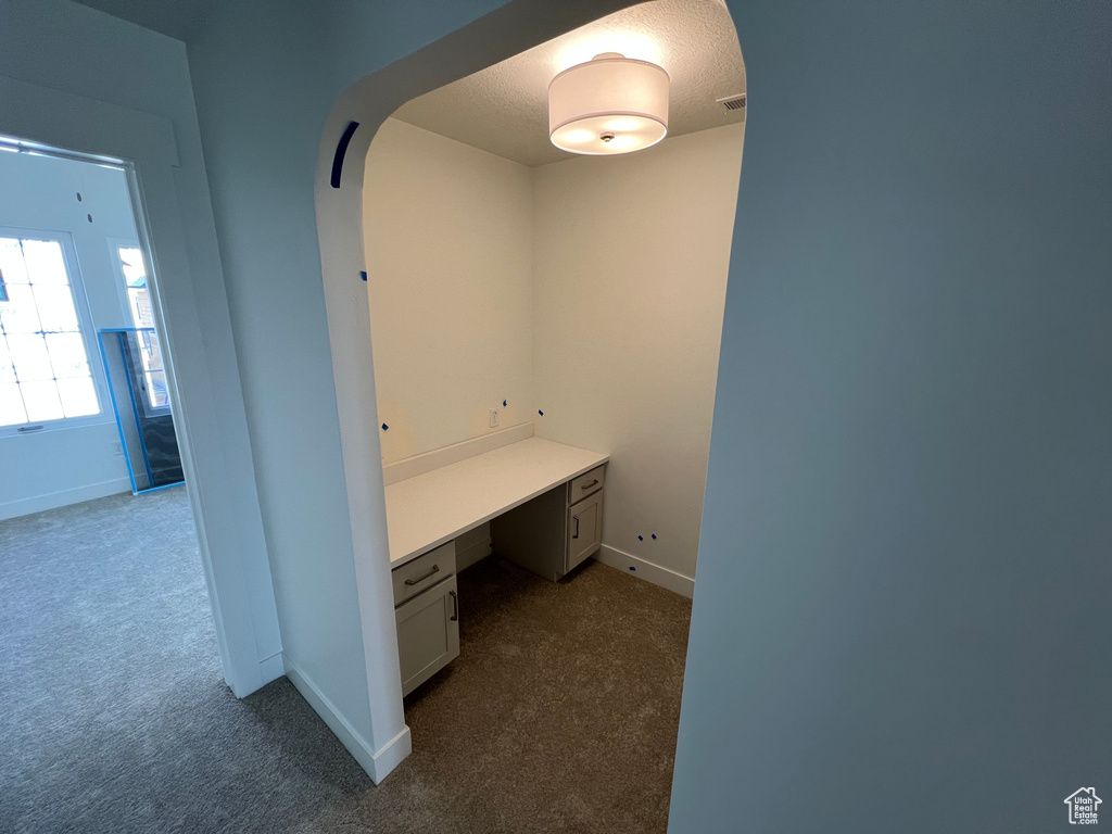 Unfurnished office with arched walkways, built in study area, dark colored carpet, and baseboards