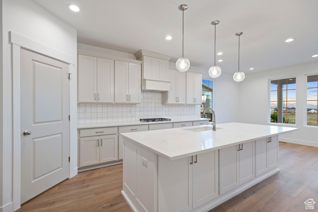 Kitchen with a sink, gas stovetop, light wood-style floors, tasteful backsplash, and plenty of natural light