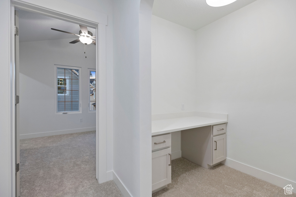 Unfurnished office featuring light carpet, arched walkways, a ceiling fan, built in study area, and baseboards