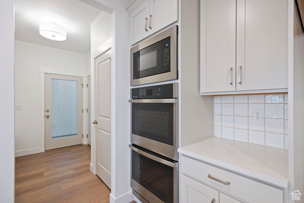 Kitchen featuring stainless steel double oven, built in microwave, tasteful backsplash, light wood-style floors, and light stone countertops