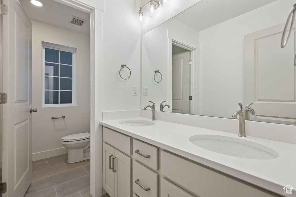 Bathroom featuring toilet, double vanity, and baseboards